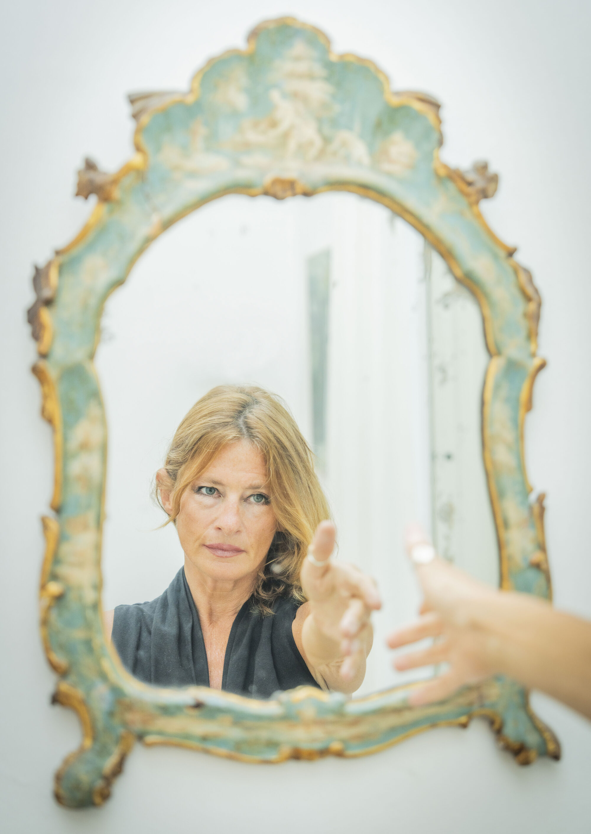 woman reachng out towards her reflection in an ornate mirror
