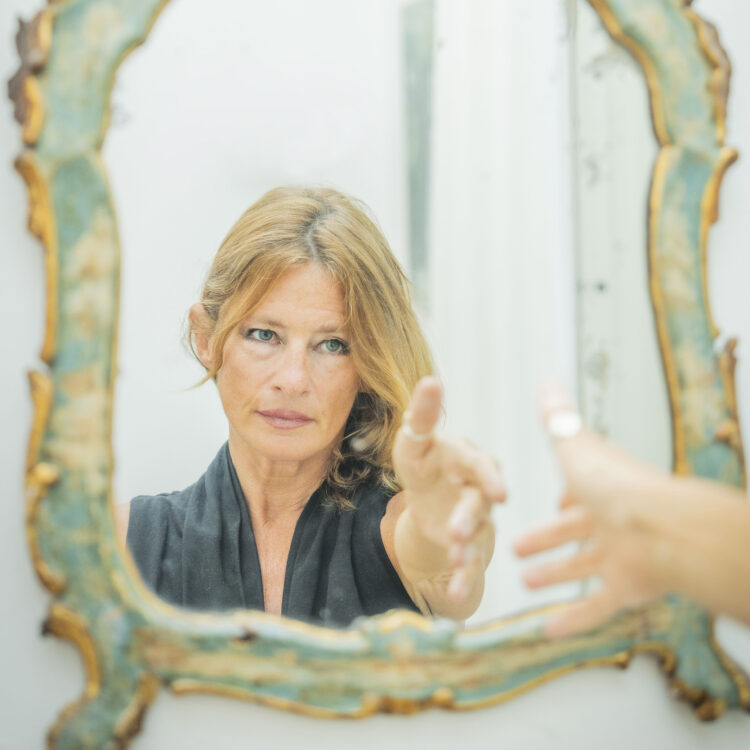 woman reachng out towards her reflection in an ornate mirror